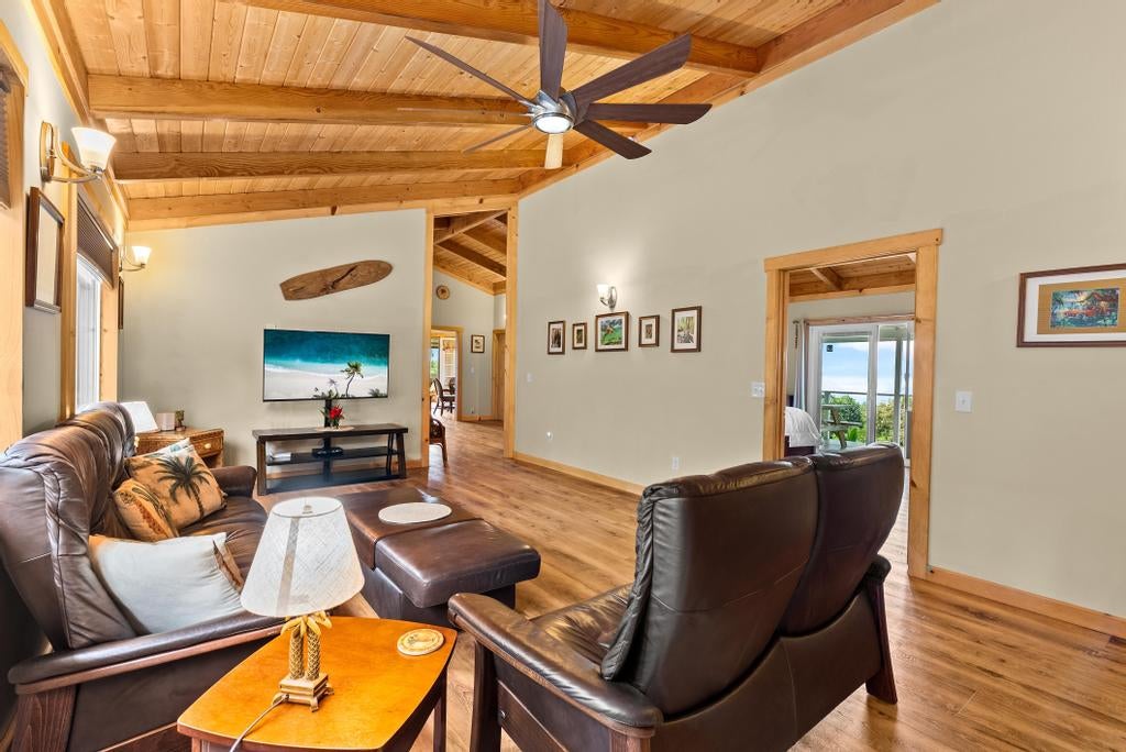 Living room with leather seating, vaulted wood ceiling, and a glimpse of ocean through the doorway.