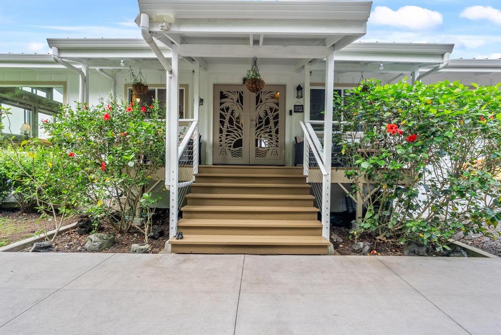 House entrance with broad wooden steps, covered porch, and carved double doors framed by flowering shrubs.