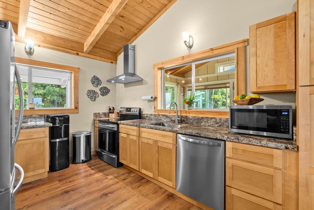 Kitchen with wood cabinets, vaulted wood ceiling, stone counters, and stainless steel appliances.