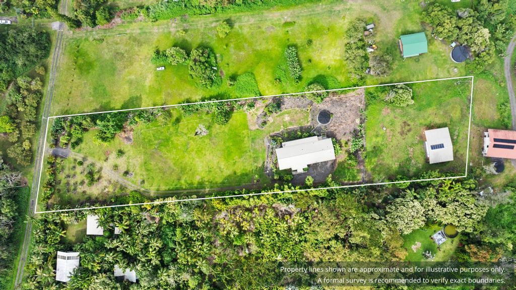 Aerial view of a grassy property outlined in white, with a house, outbuilding, and surrounding tropical vegetation.