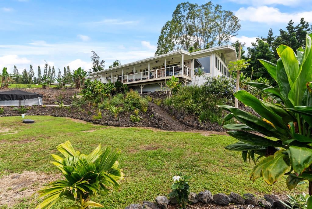 Long single-story home with a covered porch above a tropical landscaped yard.