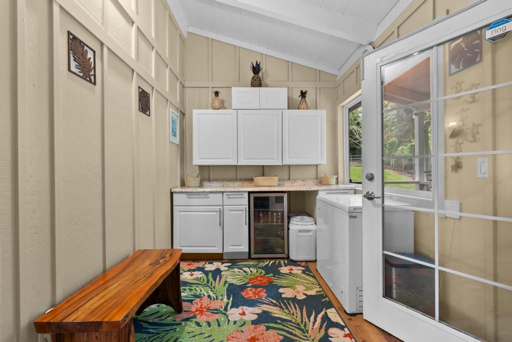 Laundry room with white cabinetry, washer and dryer, wooden bench, and tropical floral rug.