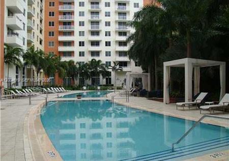 Condominium swimming pool with white cabanas, lounge chairs, and palm trees.