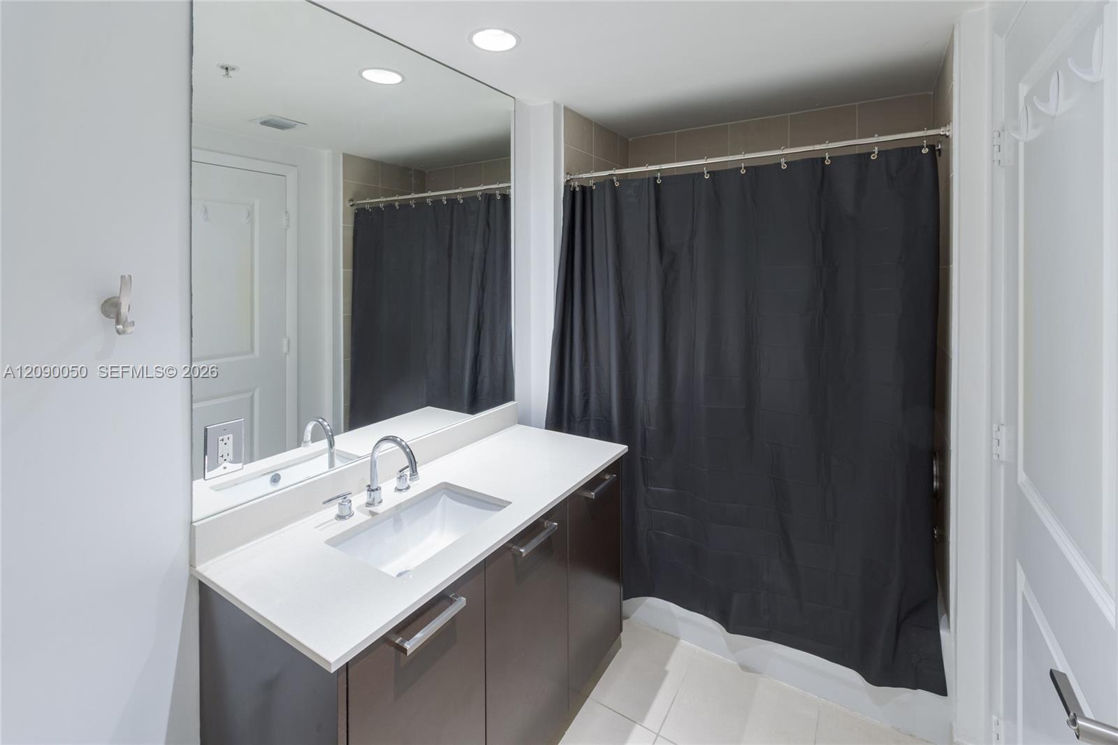 Bathroom with a long dark vanity, white countertop, large mirror, and charcoal shower curtain.
