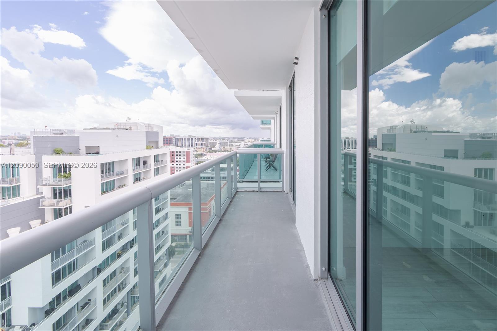 Condominium balcony with glass railing, sliding doors, and views of surrounding city buildings.