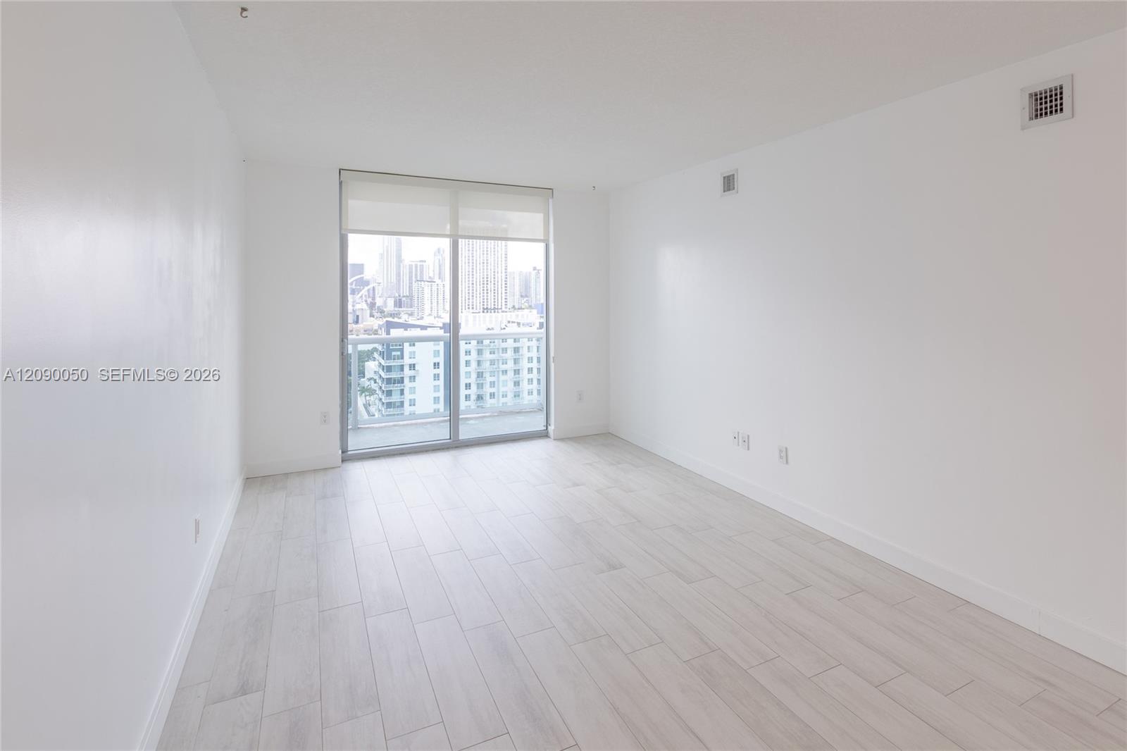 Empty apartment room with light tile floors, sliding glass doors, and a city skyline view.