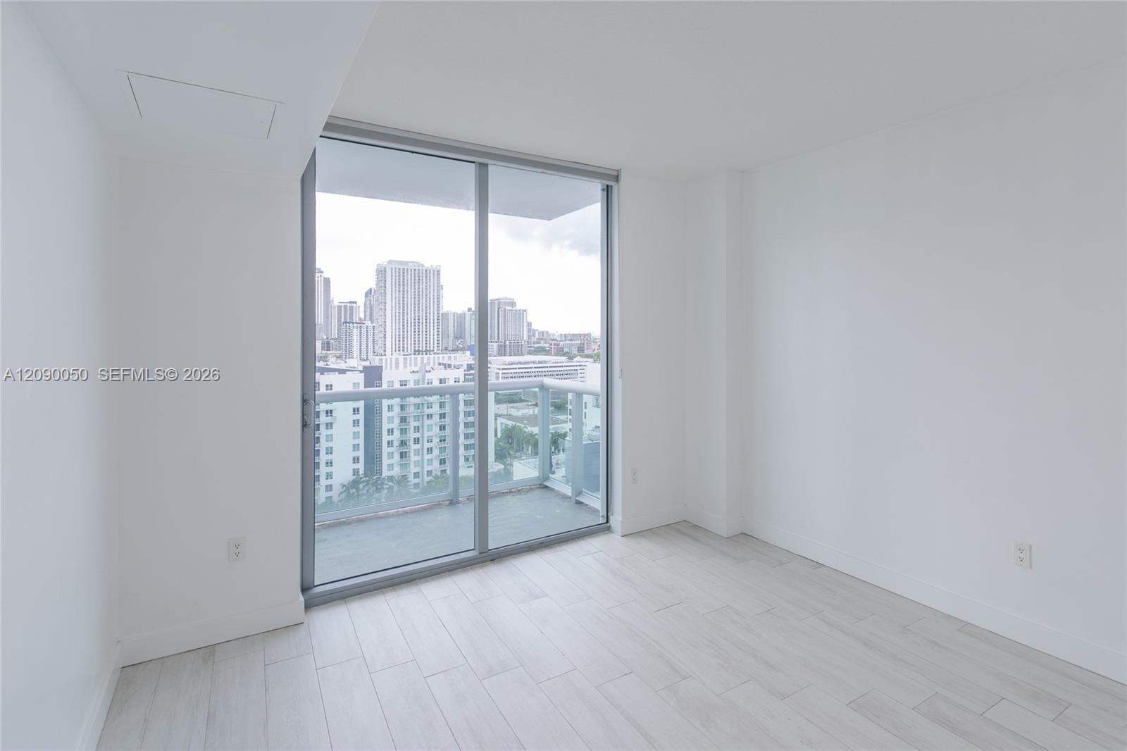 Vacant room with pale tile floors, balcony doors, and a view of the Miami skyline.