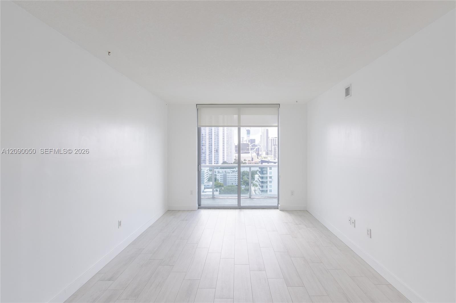 Empty condo living area with pale tile floors and sliding glass doors overlooking the city.