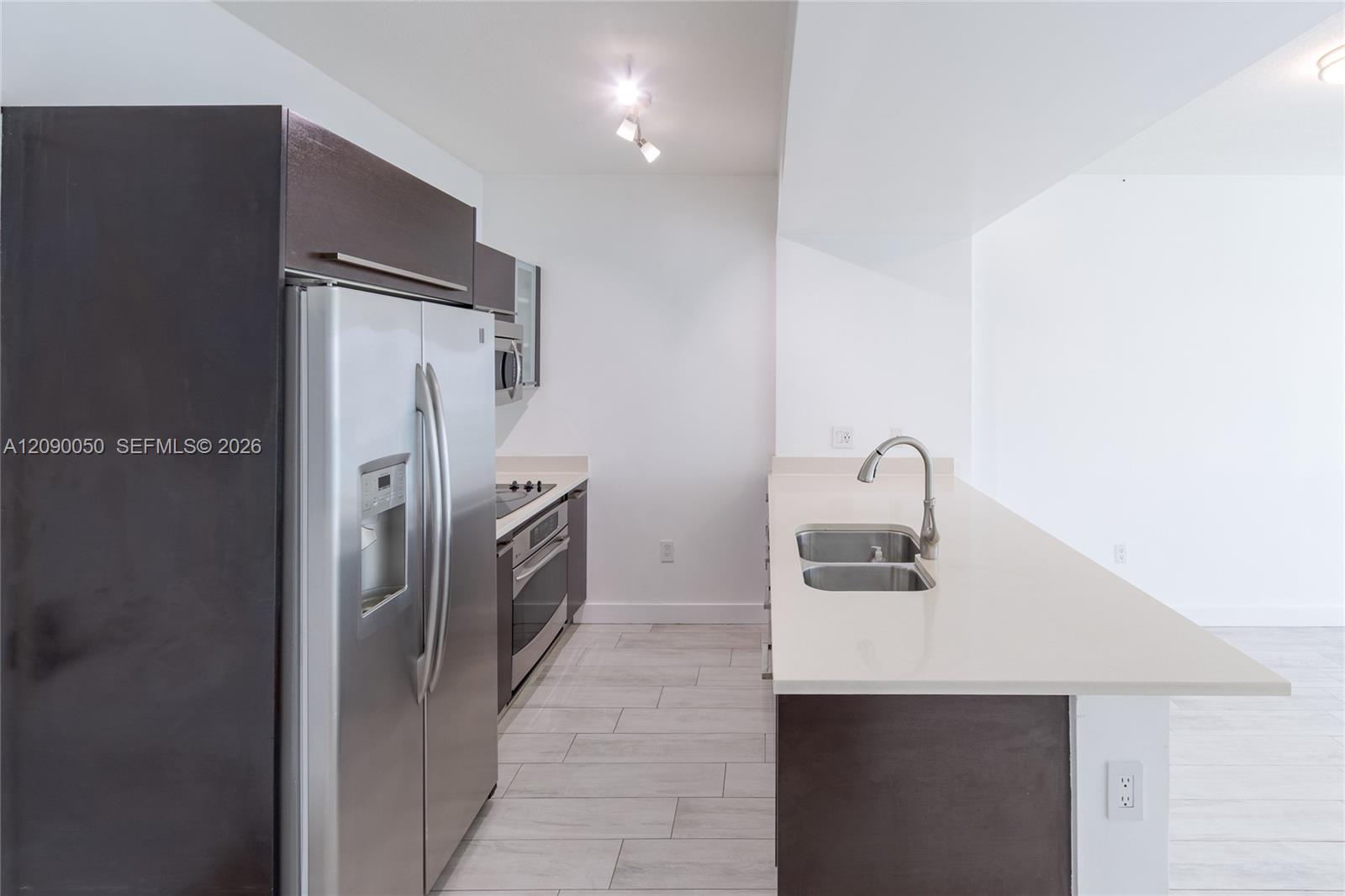 Modern kitchen with dark cabinets, stainless steel appliances, and a white peninsula with double sink.