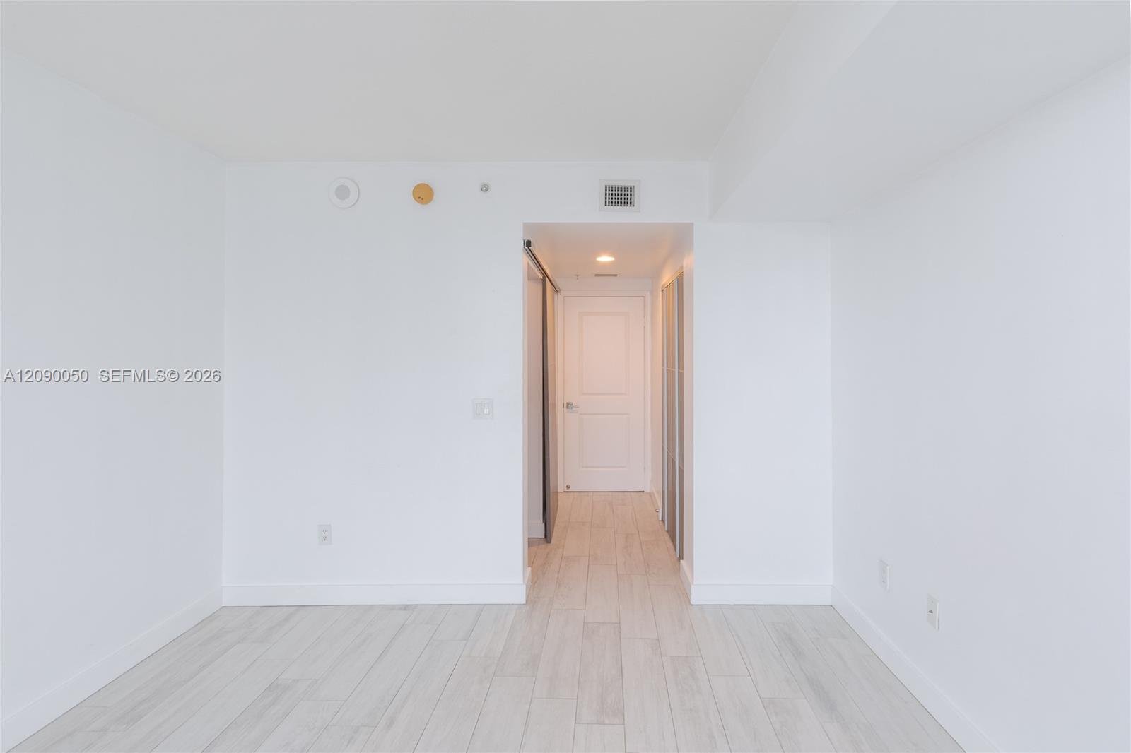 Empty white room with pale tile flooring and an open doorway to a hallway.