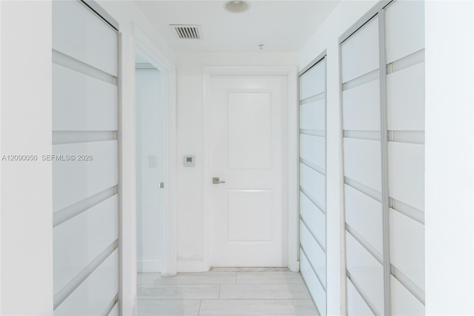 Bright white hallway with sliding closet doors on both sides and a paneled door at the end.