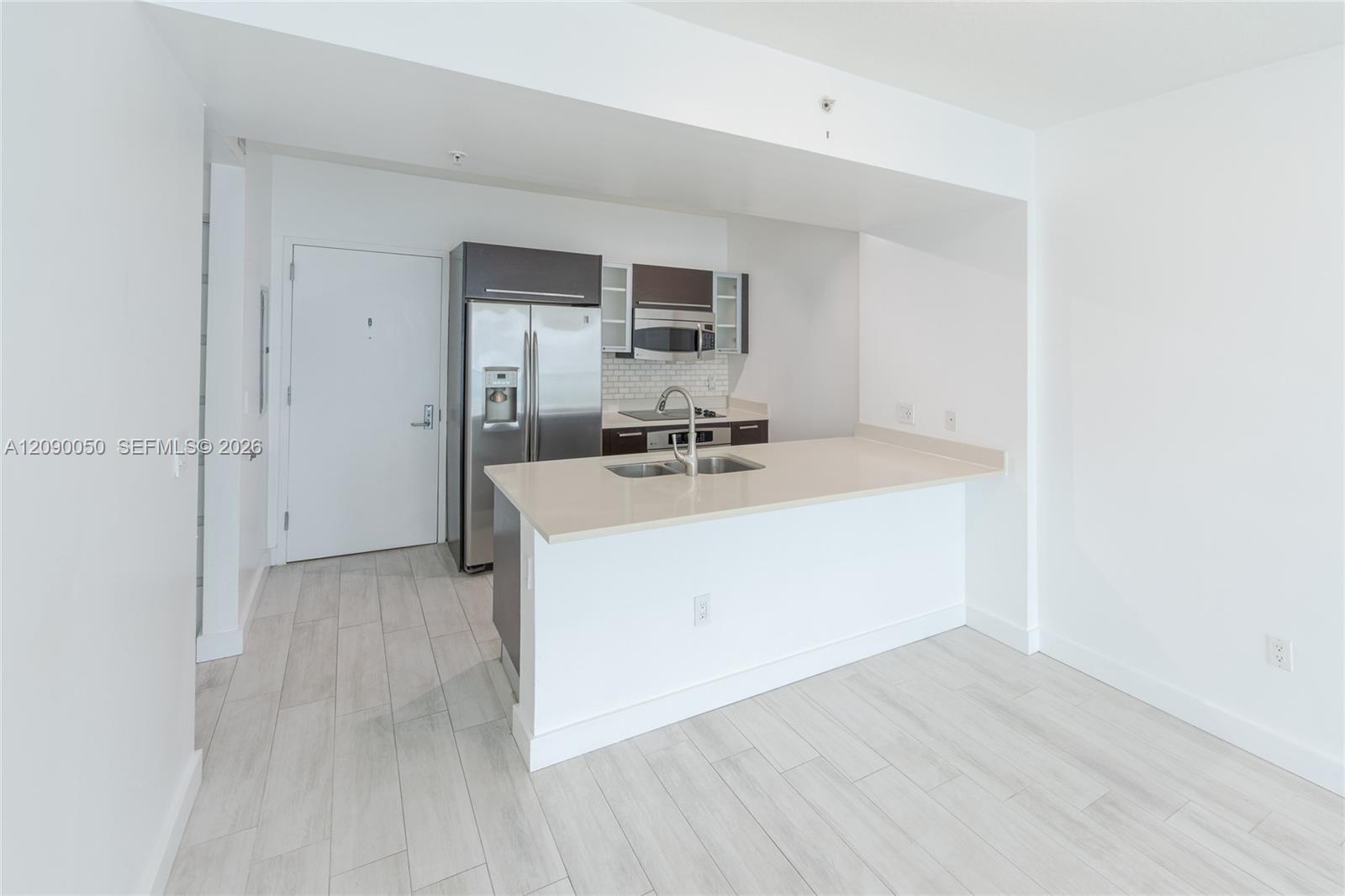 Vacant condo kitchen with a white peninsula island and stainless steel appliances.
