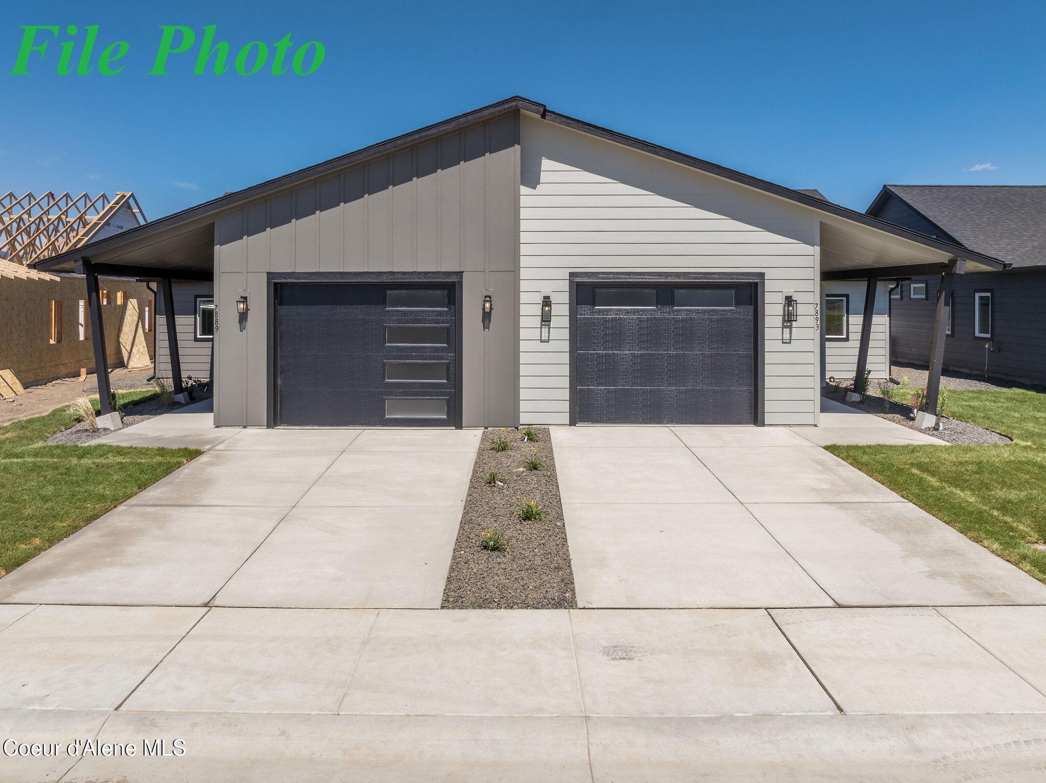 Modern gray home with two dark garage doors and a broad concrete driveway.