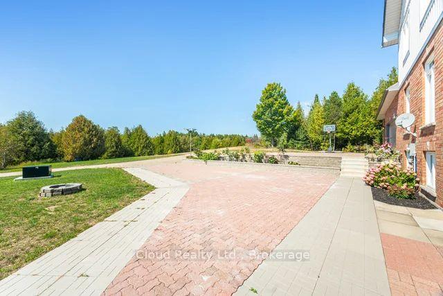 Paved patio beside a brick home, with flower beds, lawn, and trees beyond.