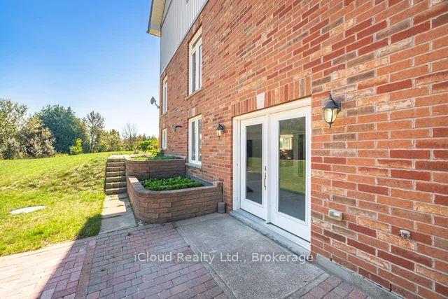 Red brick home with white patio doors, raised brick planters, and a paved terrace beside a grassy yard.