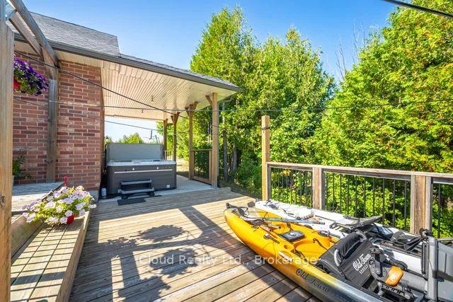 Wood deck with a covered hot tub, flower planters, and kayaks beside a tree-lined view.
