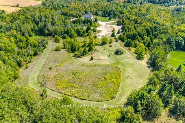 Aerial view of a wooded property with a large cleared meadow and winding track.