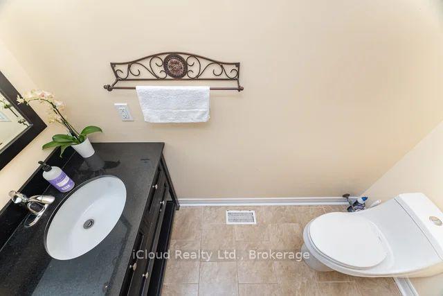 Bathroom with a dark vanity, oval sink, white toilet, and beige tiled floor.