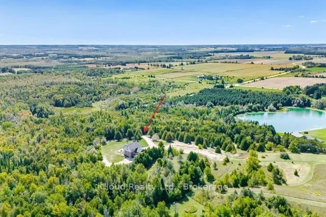 Aerial view of a rural home surrounded by woodland, with a pond and farmland nearby.