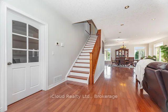 Home interior with a wood-railed staircase, hardwood floors, and dining area beyond.