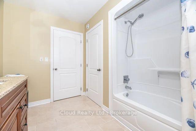 Bathroom with a white tub and shower, patterned curtain, and wooden vanity with stone countertop.