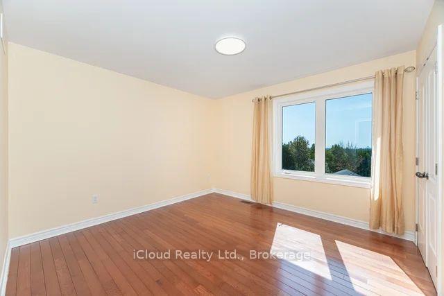 Empty room with reddish-brown hardwood floors, beige curtains, and a large sunlit window.