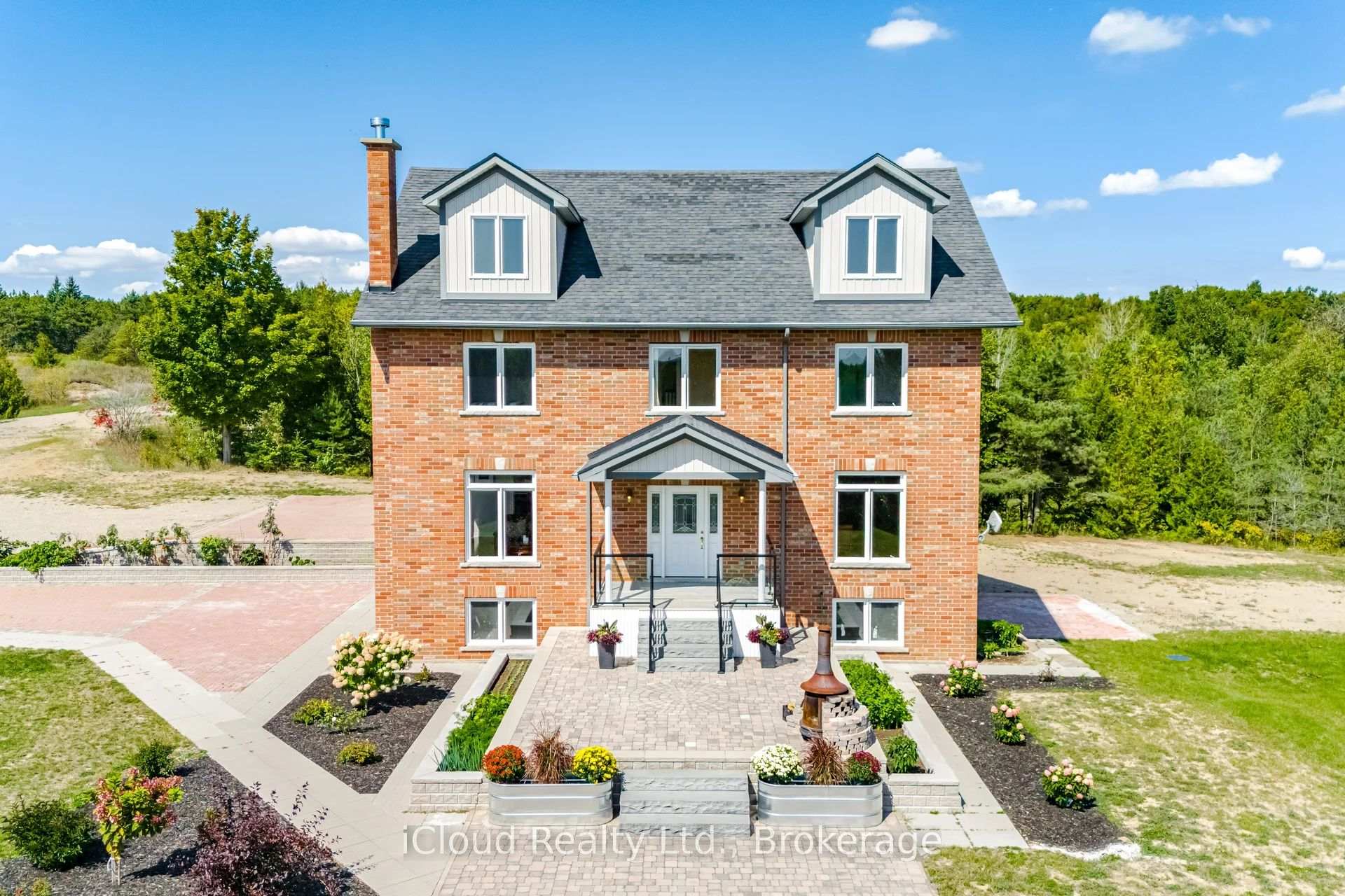 Red-brick house with two roof dormers, landscaped flower beds, and a paved front walkway.