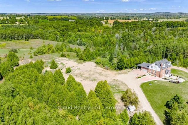 Rural home beside a broad lawn and gravel drive, surrounded by wooded acreage and open fields.
