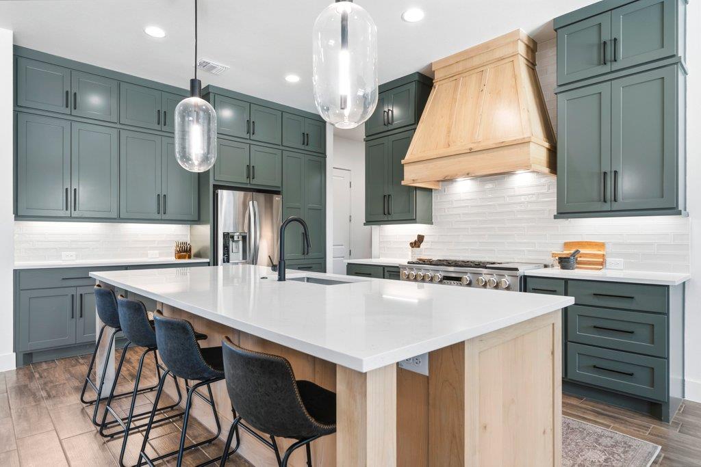 Modern kitchen with green cabinets, a large white island, and a light wood range hood.