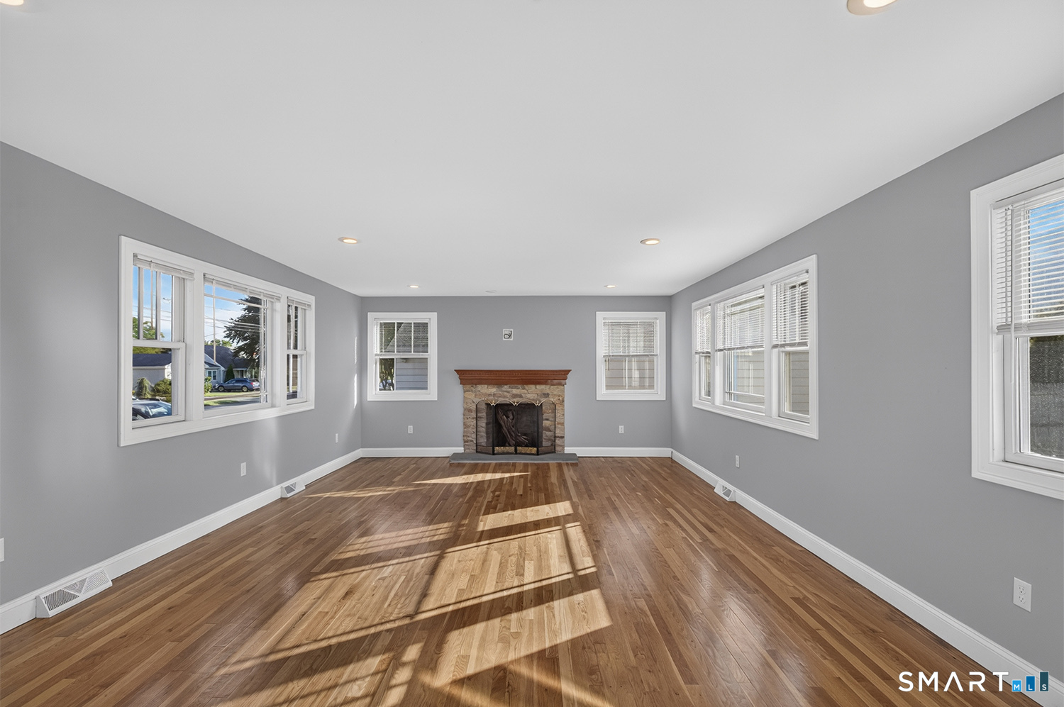Empty living room with hardwood floors, gray walls, and a stone fireplace.