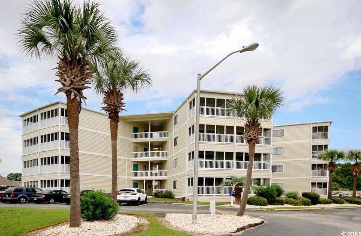 Beige multi-story condominium with white balconies, palm trees, and a front parking area.