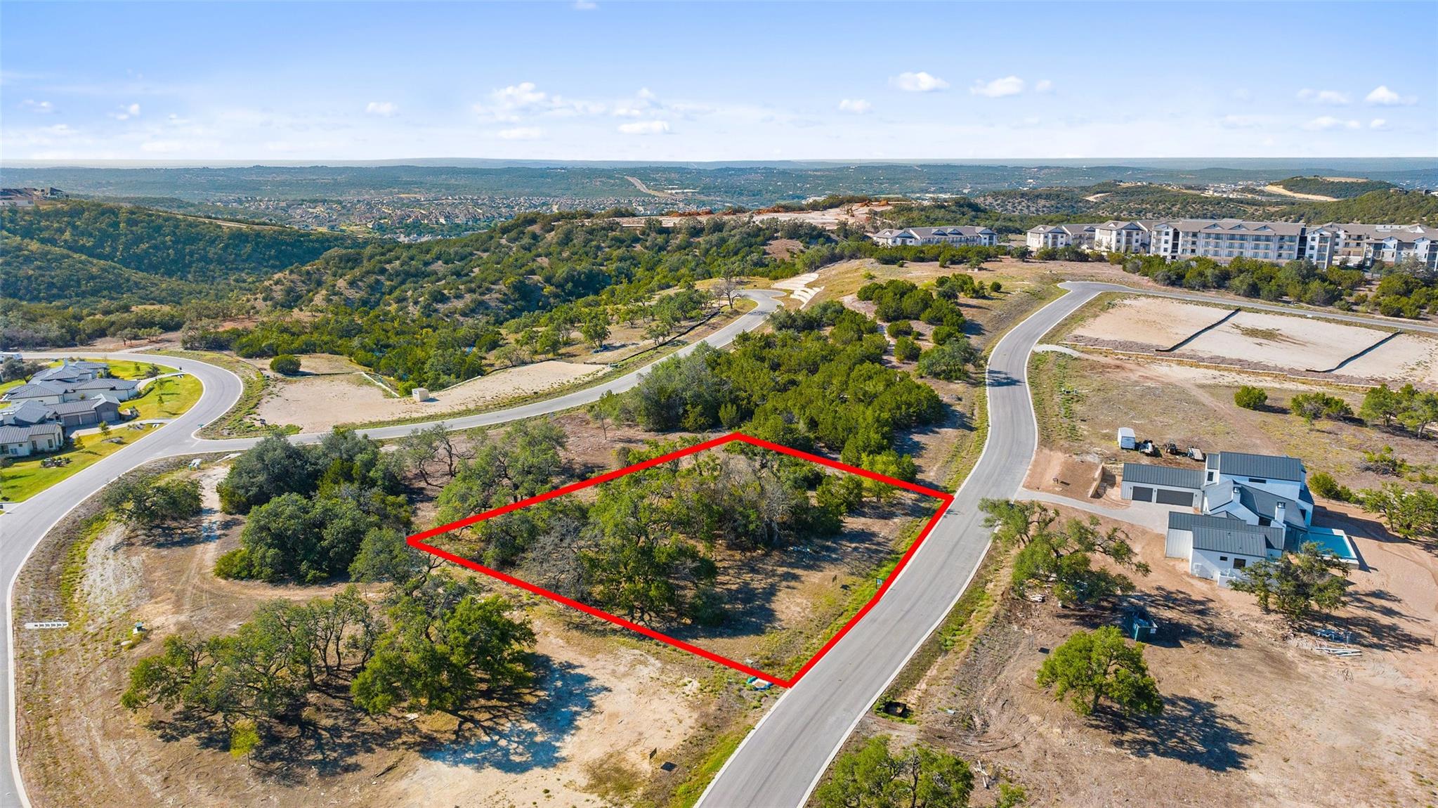 Wooded vacant lot outlined in red beside a curving road, seen from above.