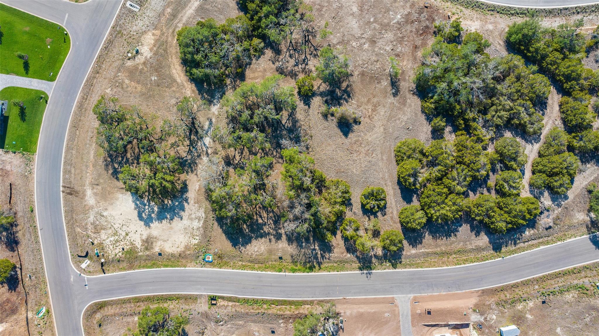 Aerial view of a cleared lot with scattered mature trees, bordered by subdivision roads.