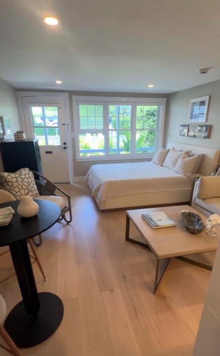 Furnished bedroom with a large bed, wide windows, and a sitting area on light wood floors.
