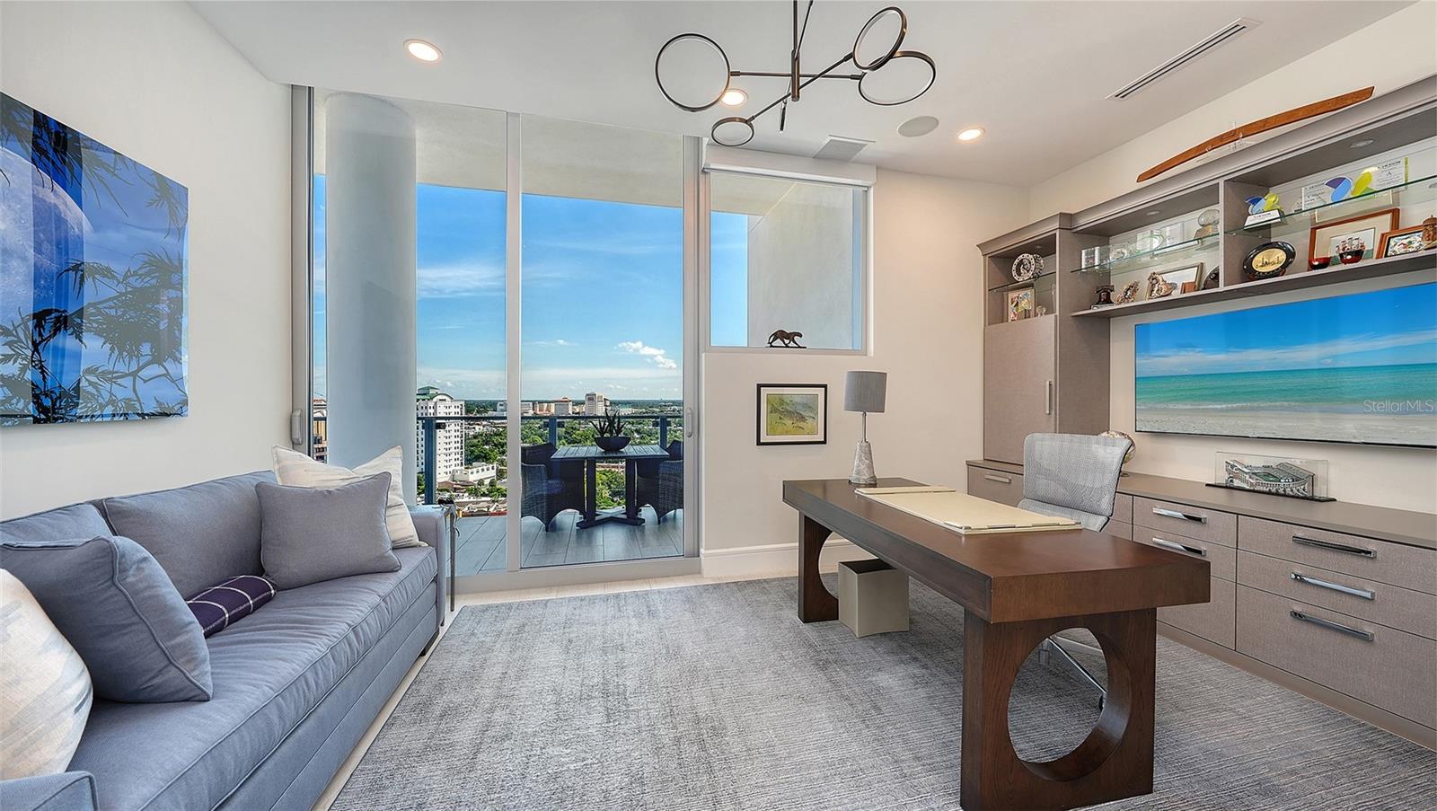 Furnished condo office with a dark wood desk and balcony windows overlooking the city.