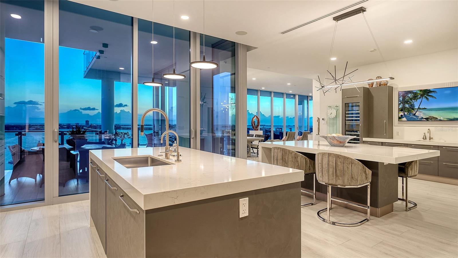 Modern condo kitchen with two stone islands and floor-to-ceiling windows overlooking the water.
