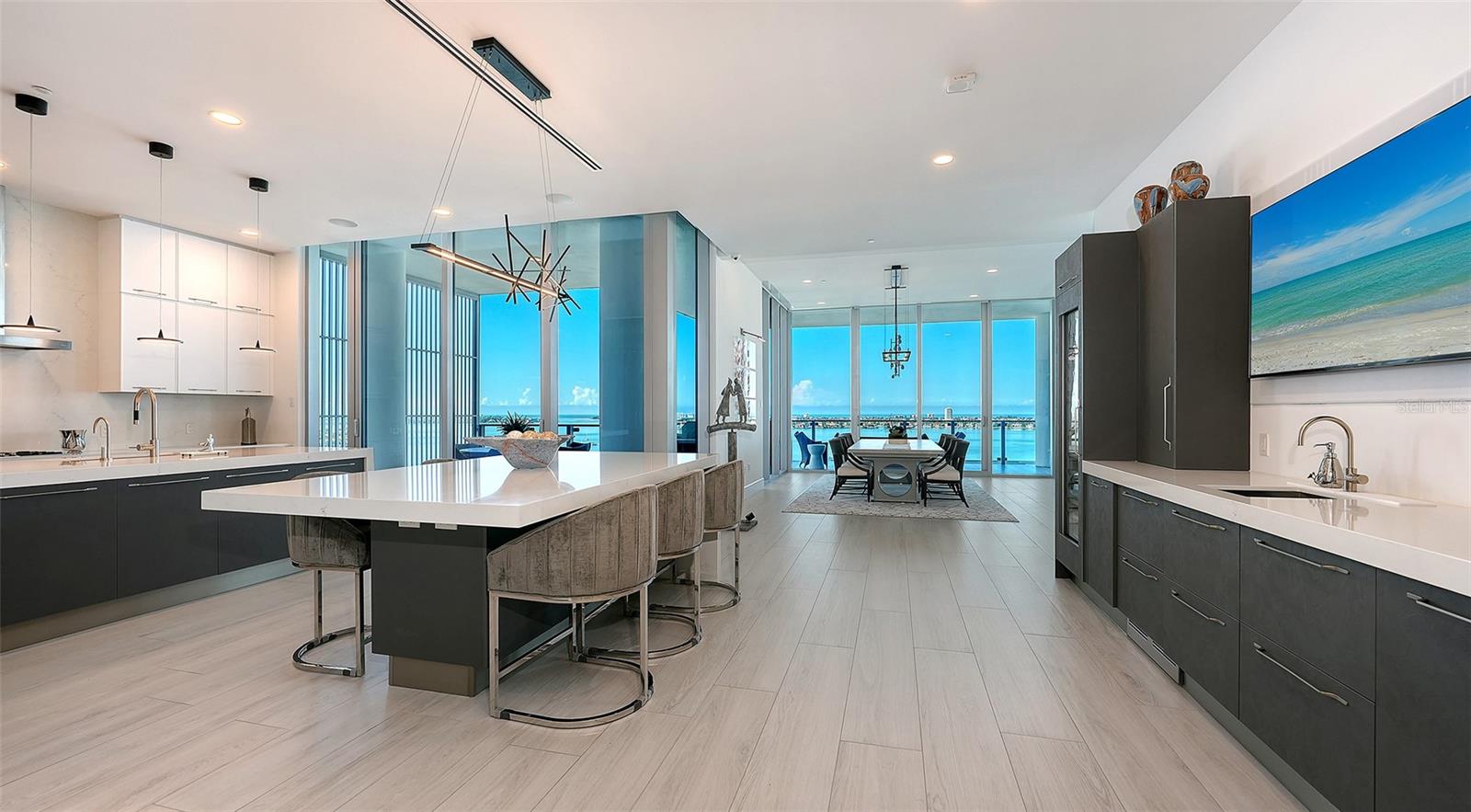 Modern kitchen and dining area with a large island and broad water views through floor-to-ceiling windows.