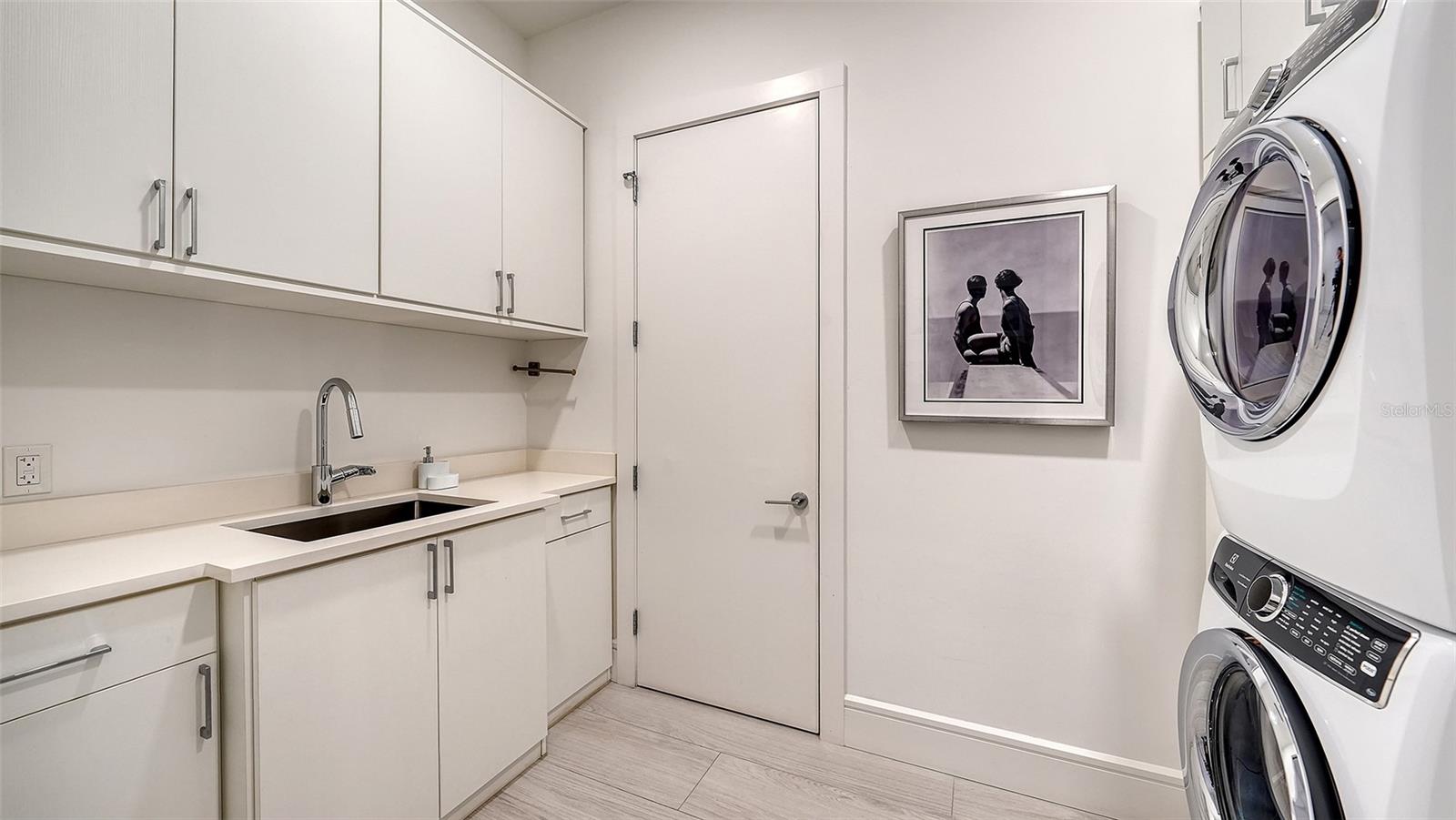 Laundry room with white built-in cabinetry, a countertop sink, and stacked front-loading washer and dryer.