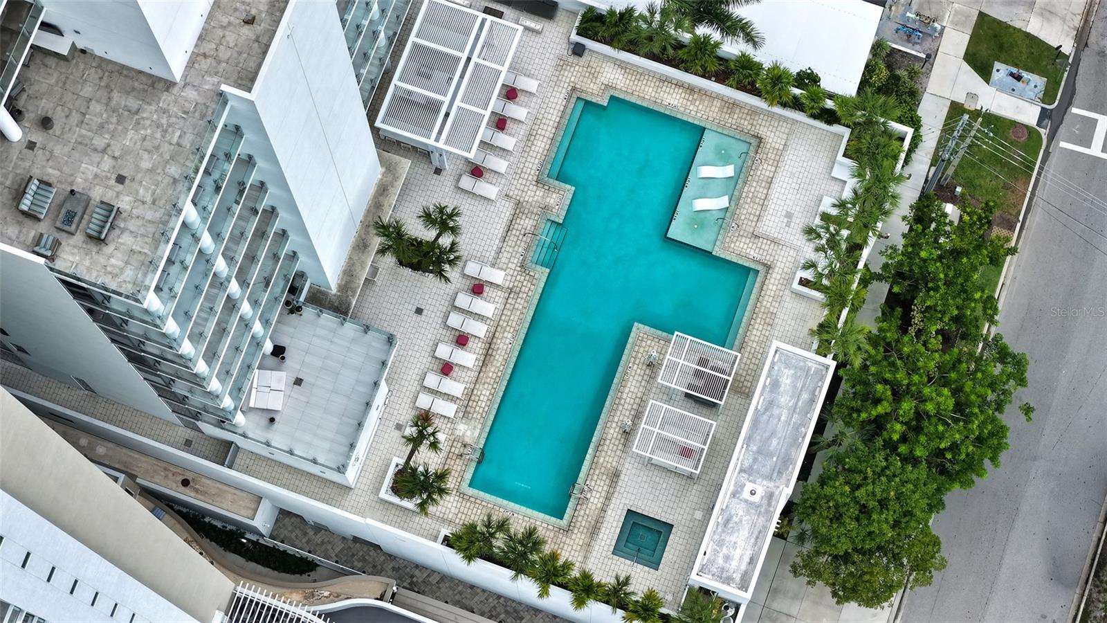 Condominium pool deck with a turquoise pool, shallow lounging area, and palm-lined seating.