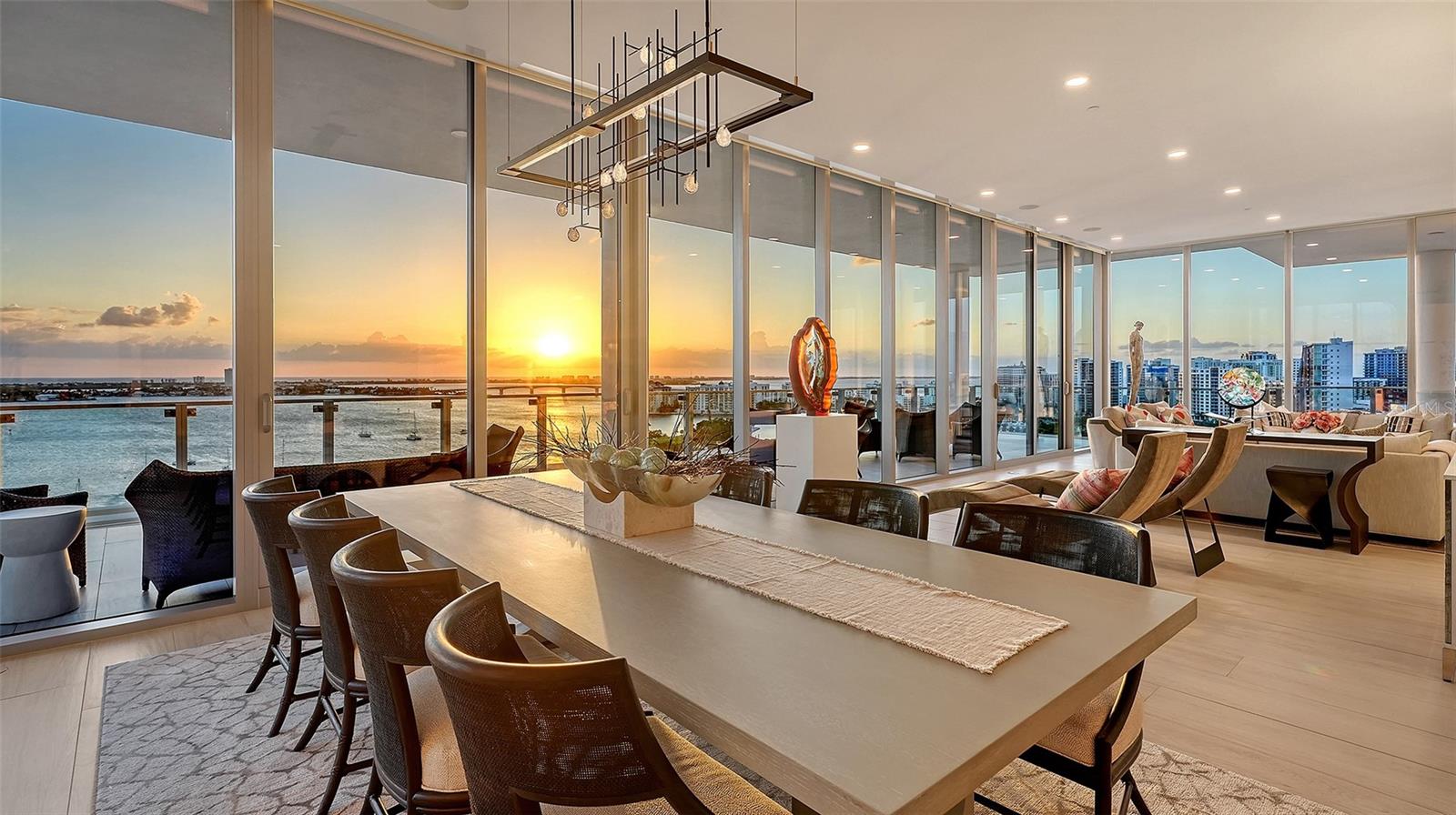 Dining and living area with floor-to-ceiling windows overlooking the bay at sunset.