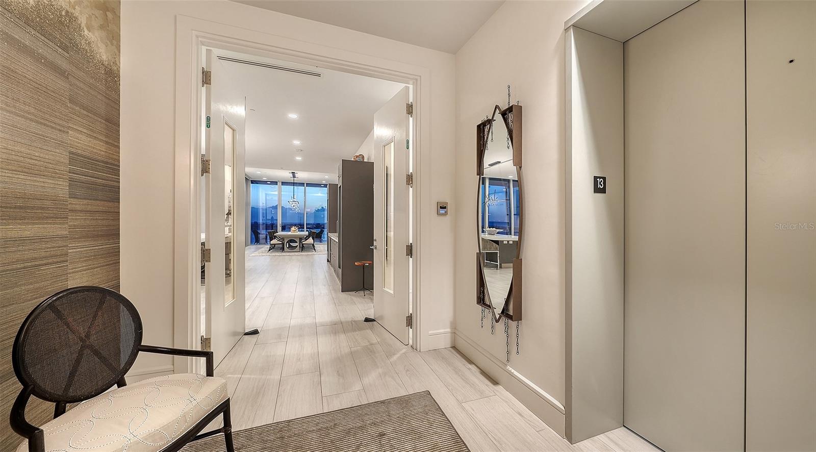 Condo entry hallway with elevator doors, a chair, and an open view toward the dining area.