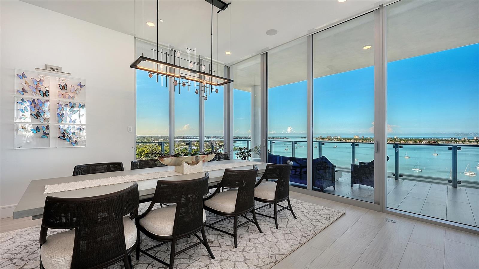 Condo dining room with floor-to-ceiling windows overlooking Sarasota Bay and a balcony with dark chairs.