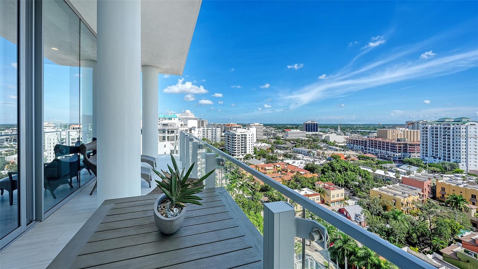 High-rise balcony with glass railings and a potted plant overlooking downtown Sarasota.