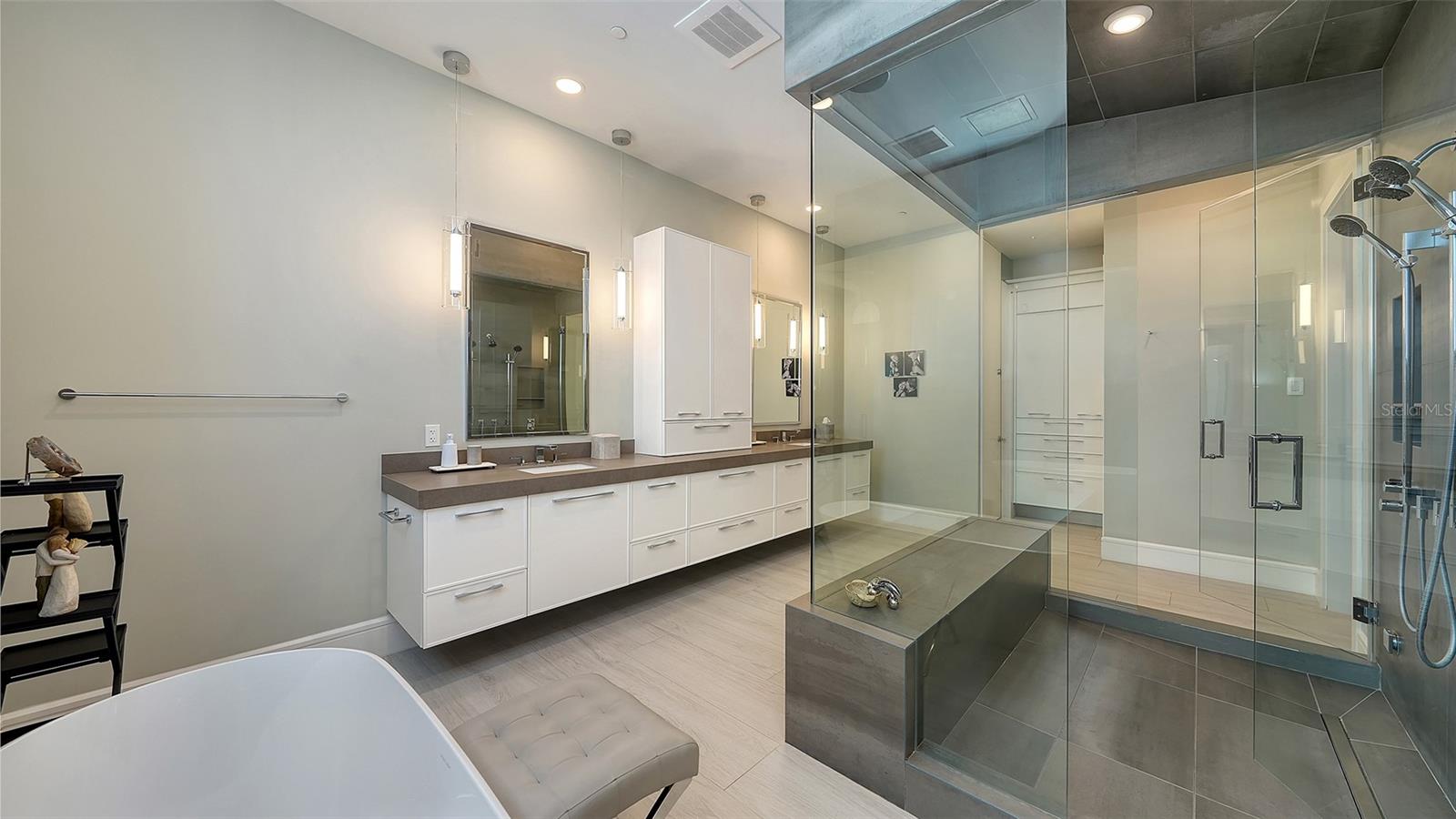 Modern bathroom with a long white vanity, glass-enclosed shower, and soaking tub.