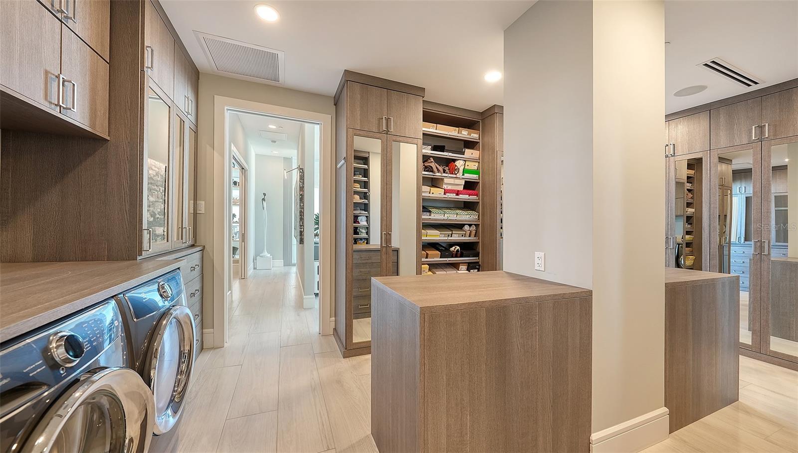 Laundry room with front-loading machines, wood cabinetry, mirrored closet doors, and a central island.