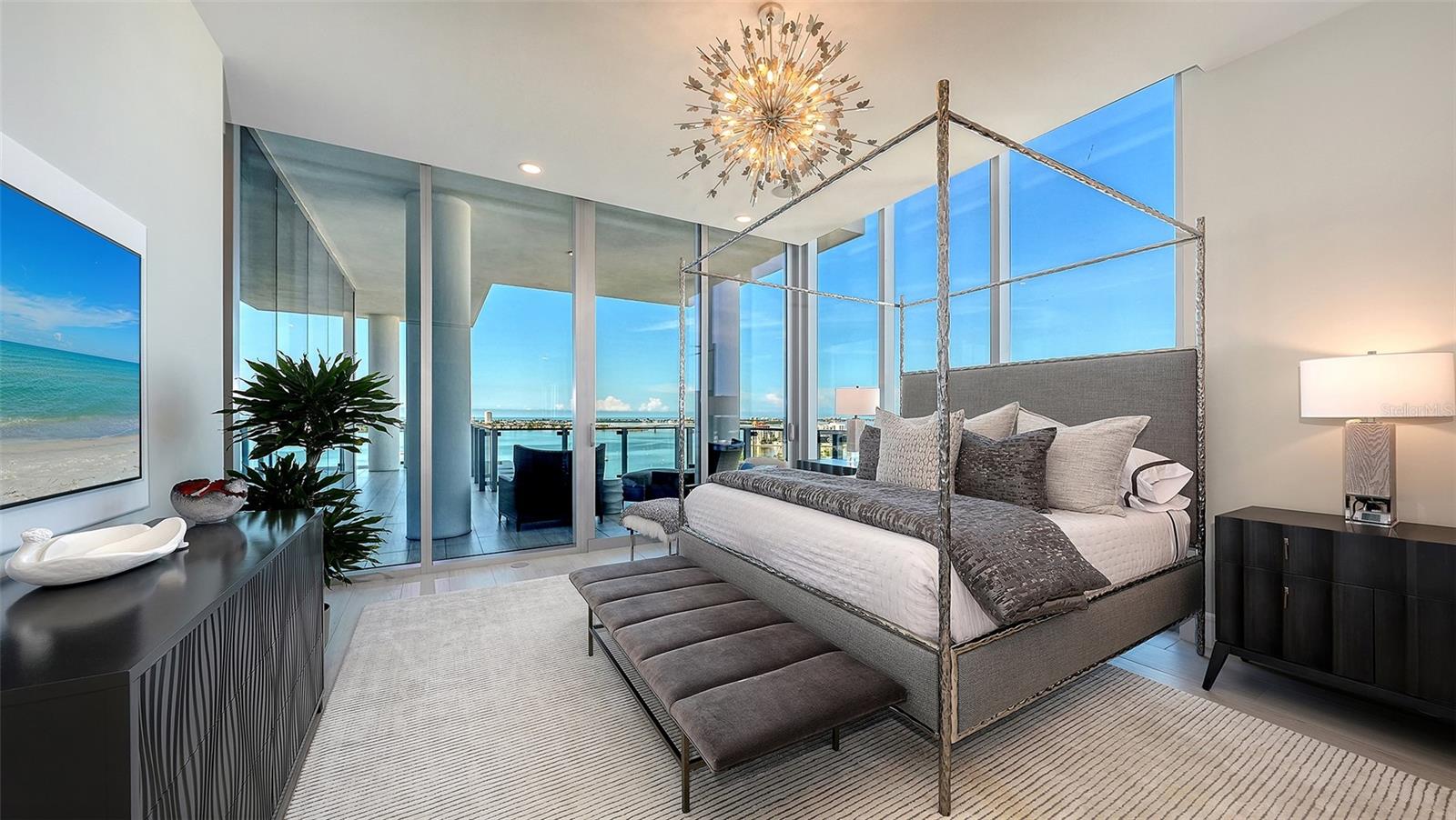 Waterfront bedroom with a gray four-poster bed and floor-to-ceiling windows overlooking the bay.