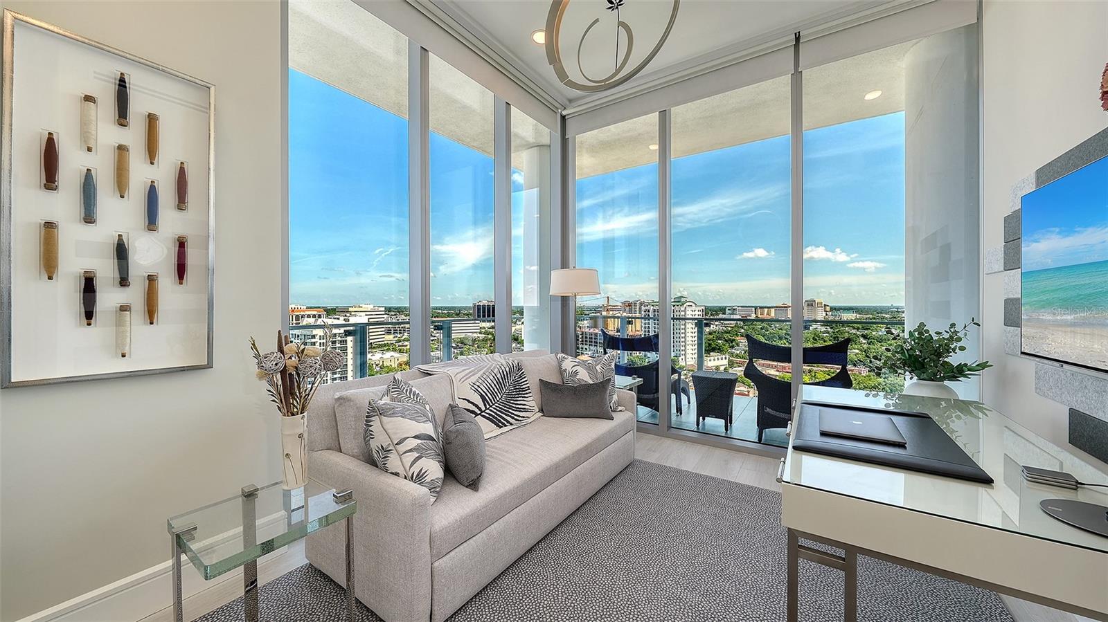 Furnished condo living room with floor-to-ceiling windows overlooking the city and a balcony.