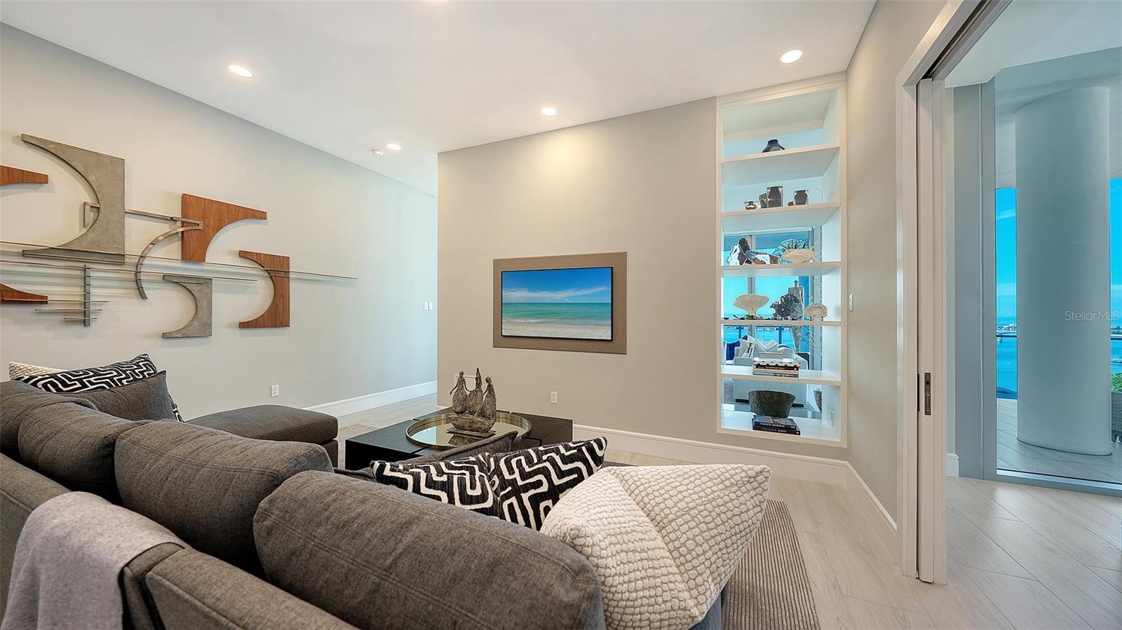 Living room with a gray sectional, built-in shelves, and sliding doors overlooking the water.