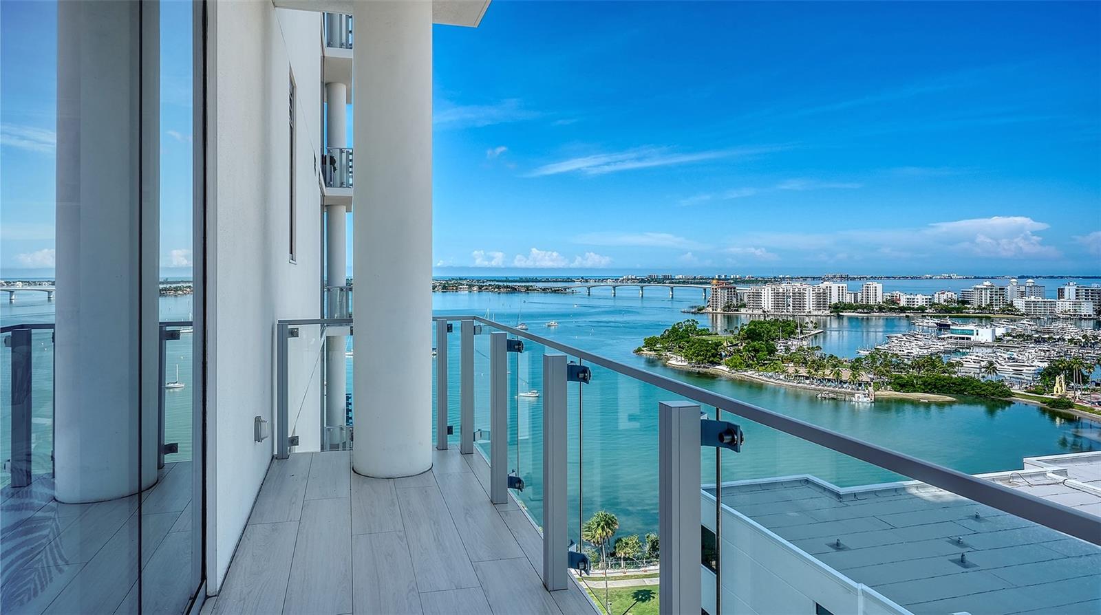 Condo balcony overlooking Sarasota Bay, with a glass railing, bridge, and marina.