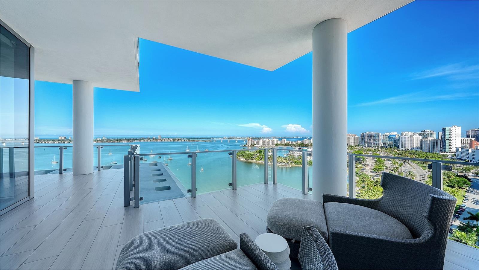 High-rise balcony overlooking bay water and Sarasota’s skyline, with glass railings and outdoor lounge seating.